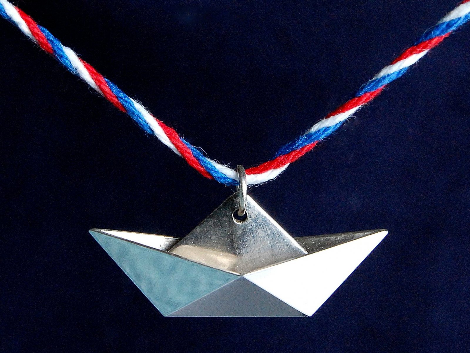 Stříbrná origami loďka navlečená na červeno-bílo-modrou nit. 